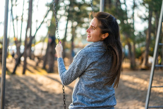 Young woman relaxing on a swing in a sunny park, embracing leisure and joy.