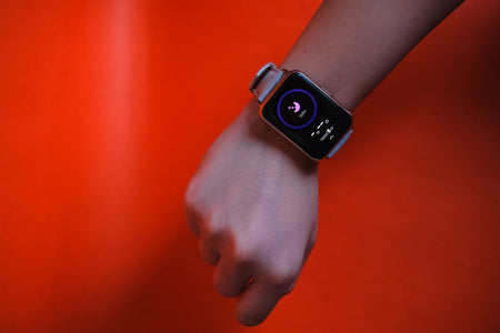 Fist wearing a smartwatch with fitness tracking display on a vibrant orange background.
