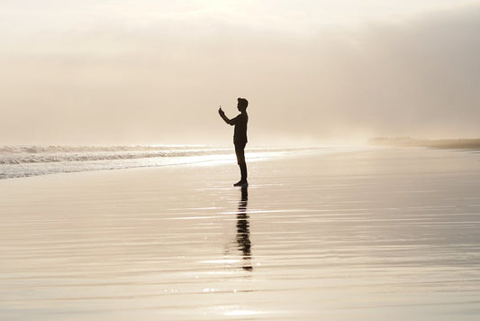 A person silhouetted on a tranquil beach at sunset, capturing a reflective moment.