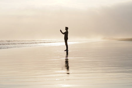 A person silhouetted on a tranquil beach at sunset, capturing a reflective moment.
