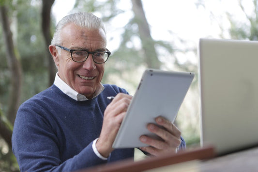 Senior man enjoying modern technology while using a tablet outdoors, smiling and engaged.