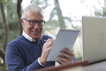 Senior man enjoying modern technology while using a tablet outdoors, smiling and engaged.