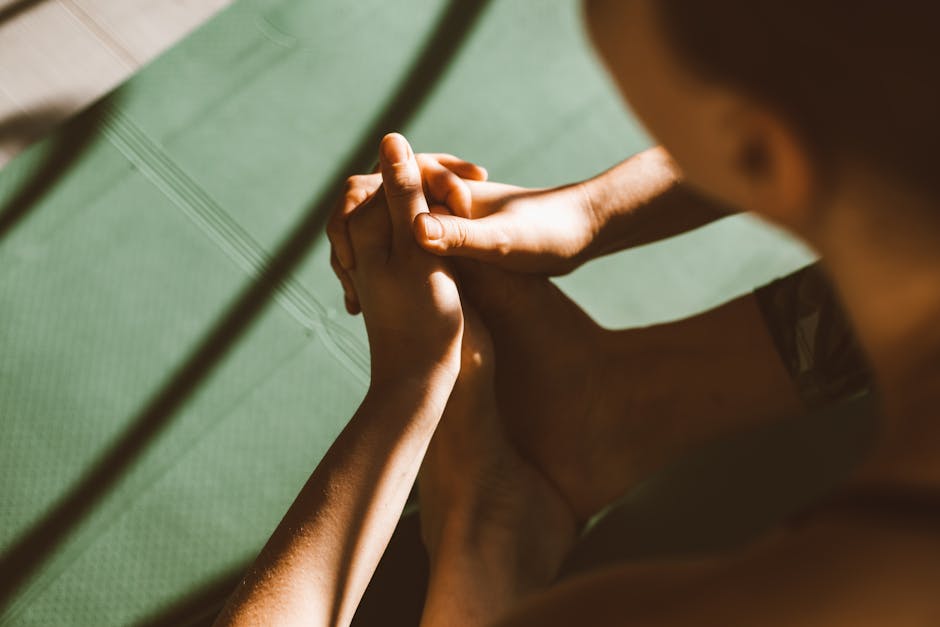 Artistic close-up of hands clasped on feet during exercise on a green mat.