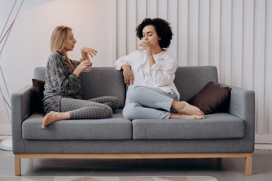 Two women enjoy a relaxing conversation with drinks on a modern sofa indoors.