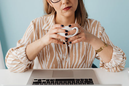 A woman enjoying a coffee break at her desk, wearing a stylish striped shirt. Ideal for lifestyle themes.