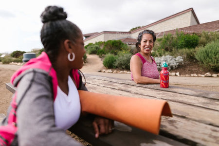 Two women enjoying a relaxing day outdoors after yoga with a mat and water bottle.